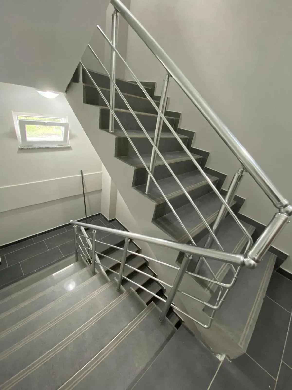 Apartman merdiven boşluğunda iki kat boyunca devam eden parlak alüminyum küpeşte, sahanlıkta dirsekle dönüyor