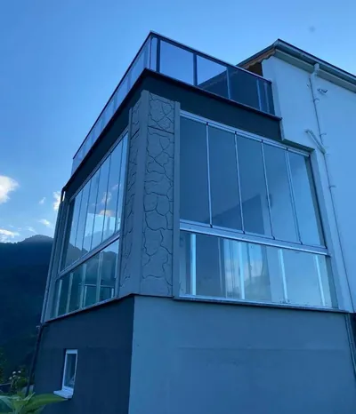 Köşe dönen beyaz profilli cam balkon ve üst çatı terasındaki cam korkuluk aynı cephede birlikte uygulanmış