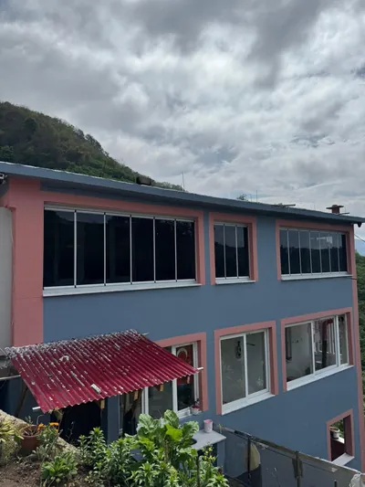 Yamaçta konumlanan iki katlı evin üst katında beyaz profilli katlanır cam balkon uygulaması