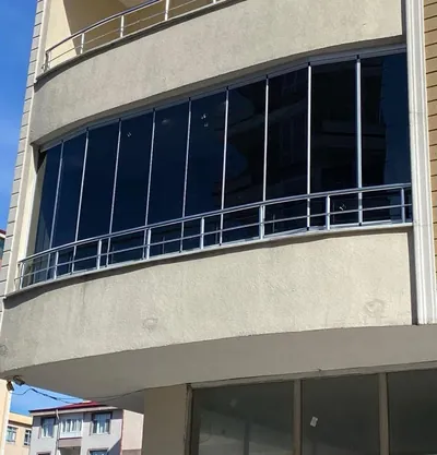 Oval çıkma balkona uygulanmış füme camlı katlanır sistem, mat gri profiller kavisi kesintisiz takip ediyor