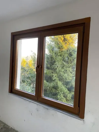 Ceviz ahşap desenli PVC çift kanat pencere, bantları sökülmüş halde camların arkasında çam ağaçları